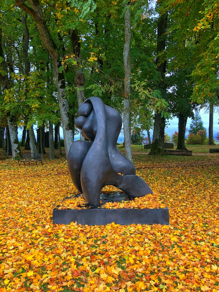 Oeuvre "mother and child" de Manuel Carbonell recouverte de feuilles orangées en automne.