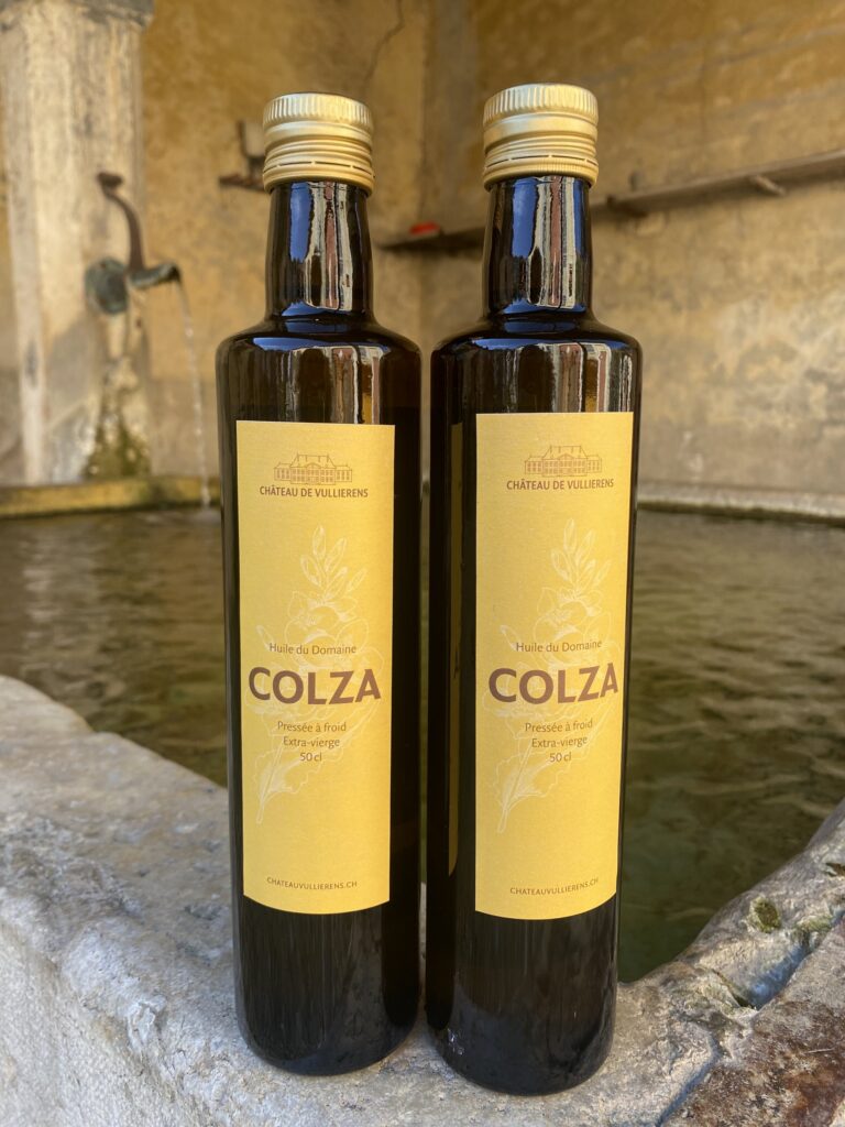 2 bouteilles d'huile de Colza du domaine posées sur le rebord de la fontaine du Château de Vullierens.