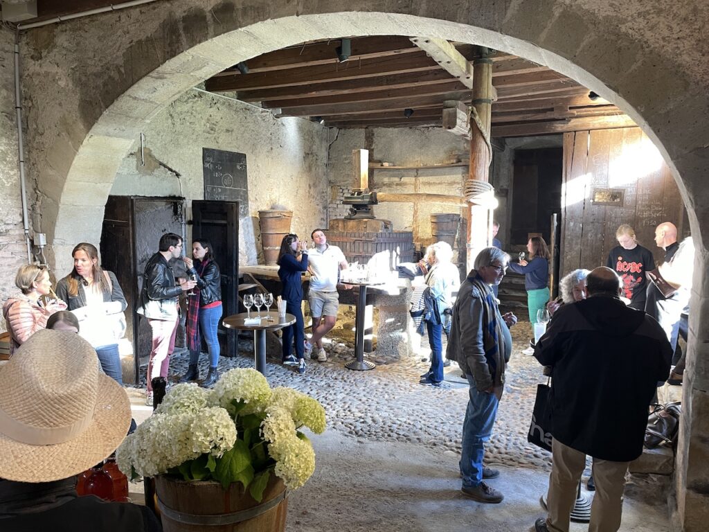 Dégustation de vins public dans la cave historique du Château de Vullierens, debout autour du pressoir d'origine.